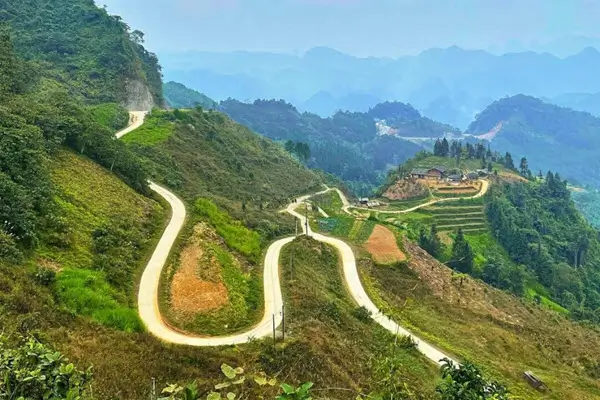 Vista aérea de una carretera montañosa sinuosa en el bucle de Ha Giang, Vietnam, con acantilados empinados y valles verdes exuberantes.